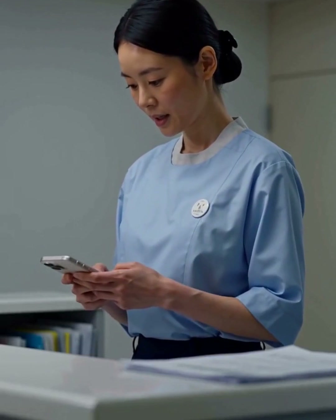 受付スタッフがカウンターでスマートフォンを持ち、患者の訳文を確認している