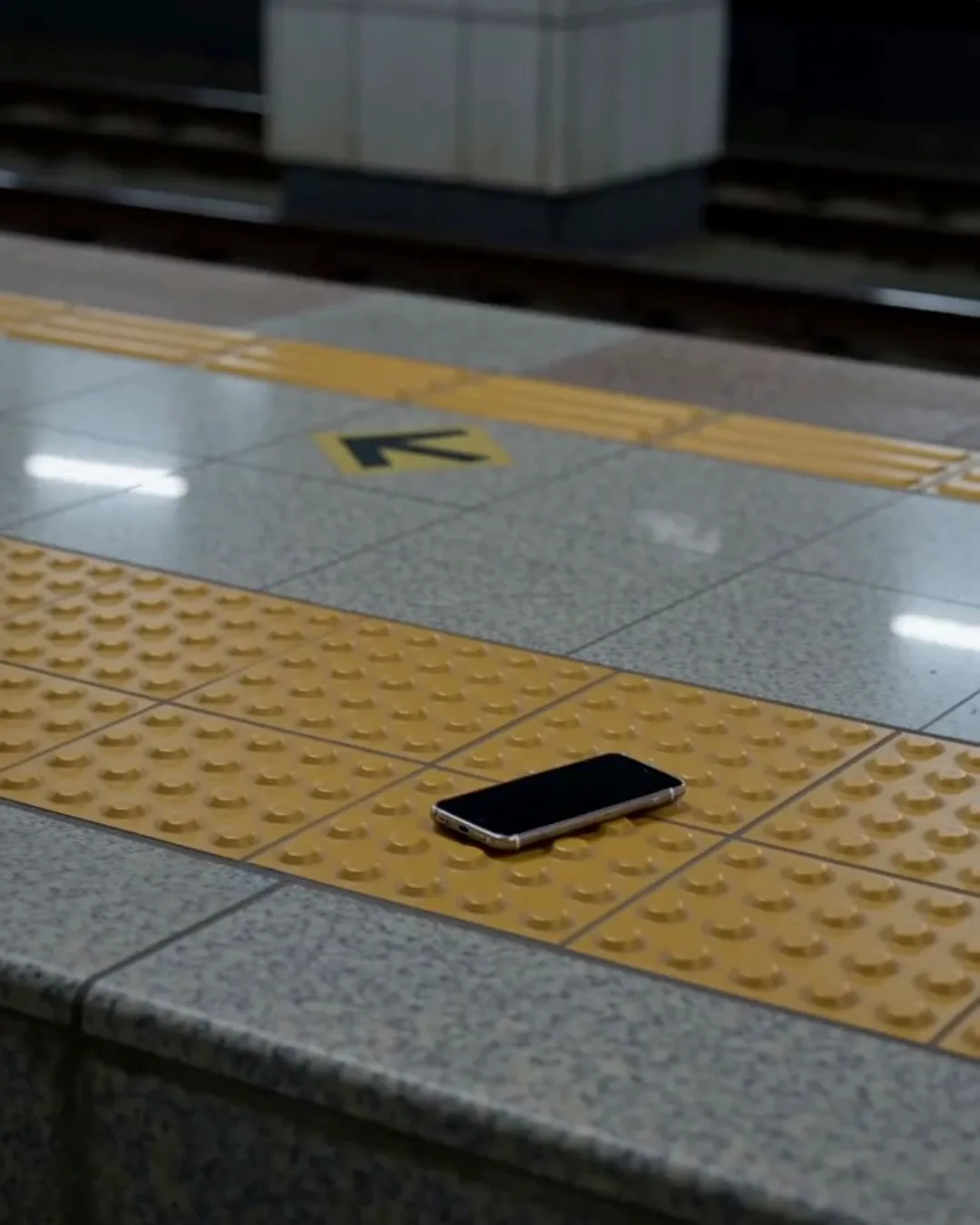 地下鉄のホームの黄色い点字ブロックの上に置かれたスマートフォン