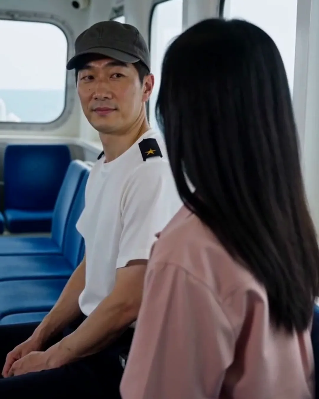 フェリーの客室で、船員の男性と外国人の女性乗客が座席の横で話している