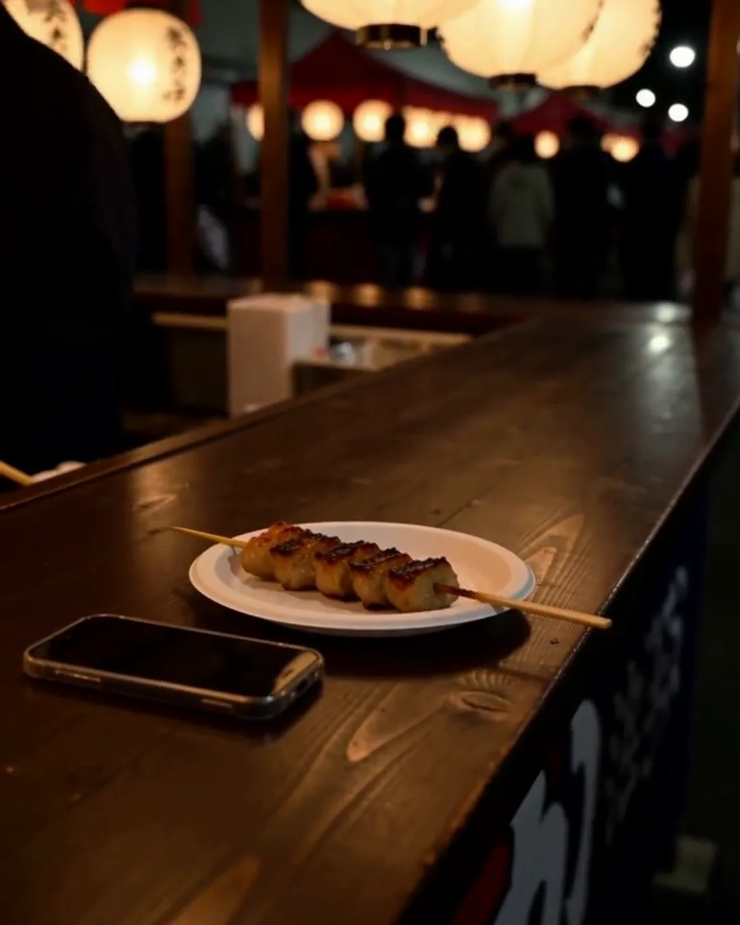 夜の屋台のカウンターに置かれた、焼き鳥の皿とスマートフォン