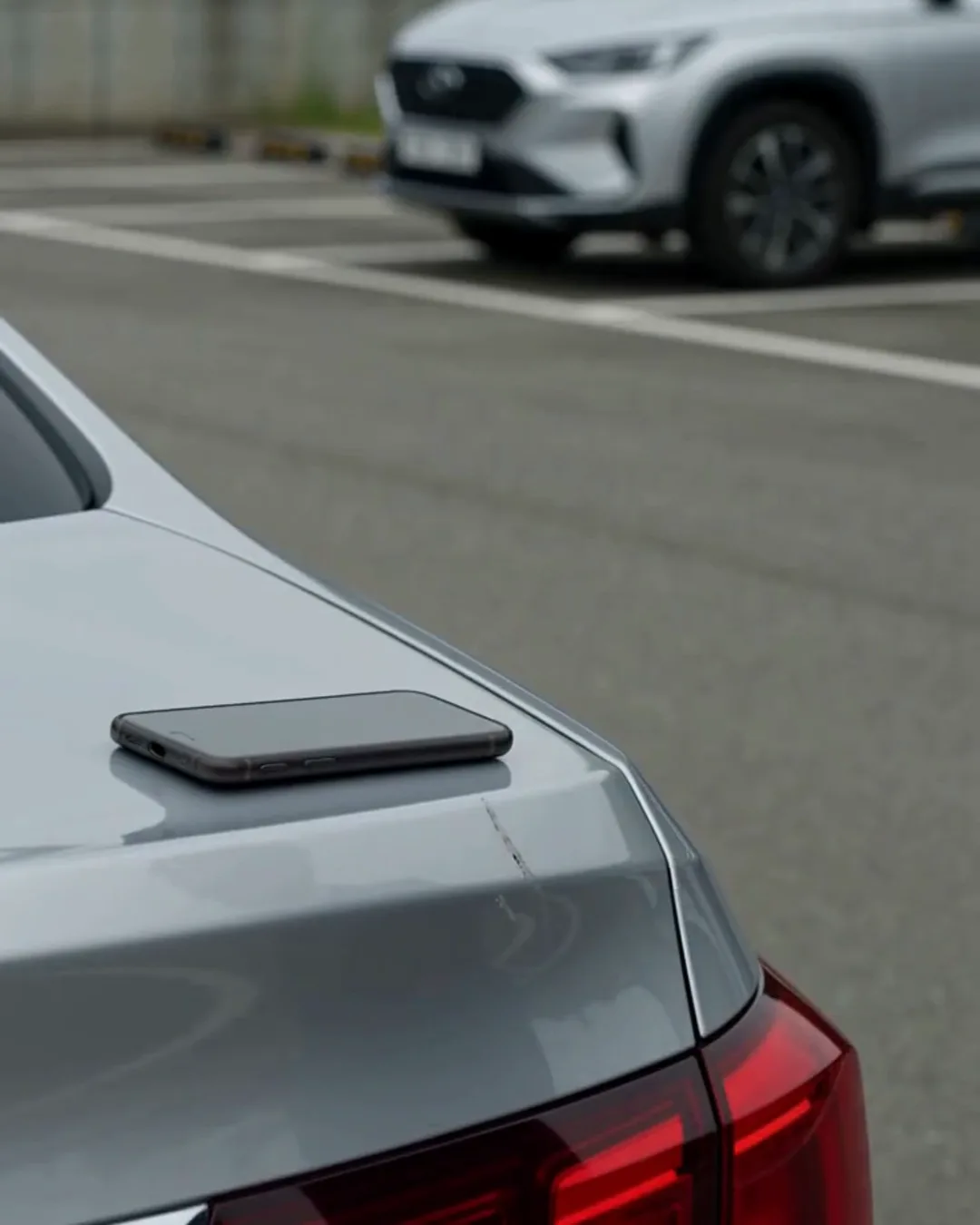 駐車場に止まった白い車の後部と、その上に置かれたスマートフォン