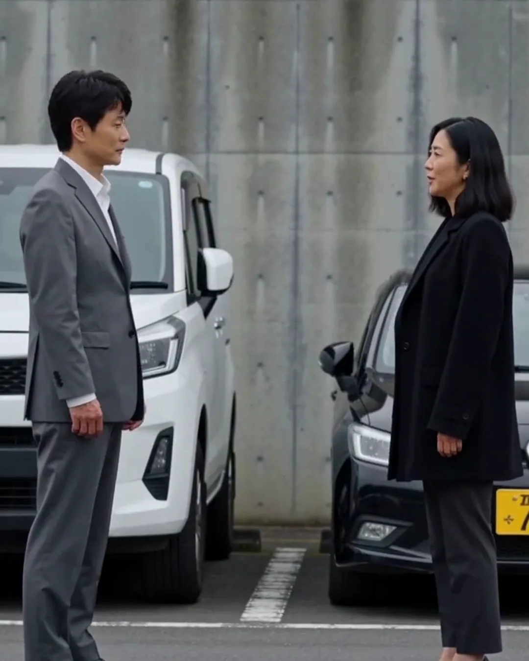 駐車場で、スーツの男性と外国人の女性運転手が接触した車の前で話している
