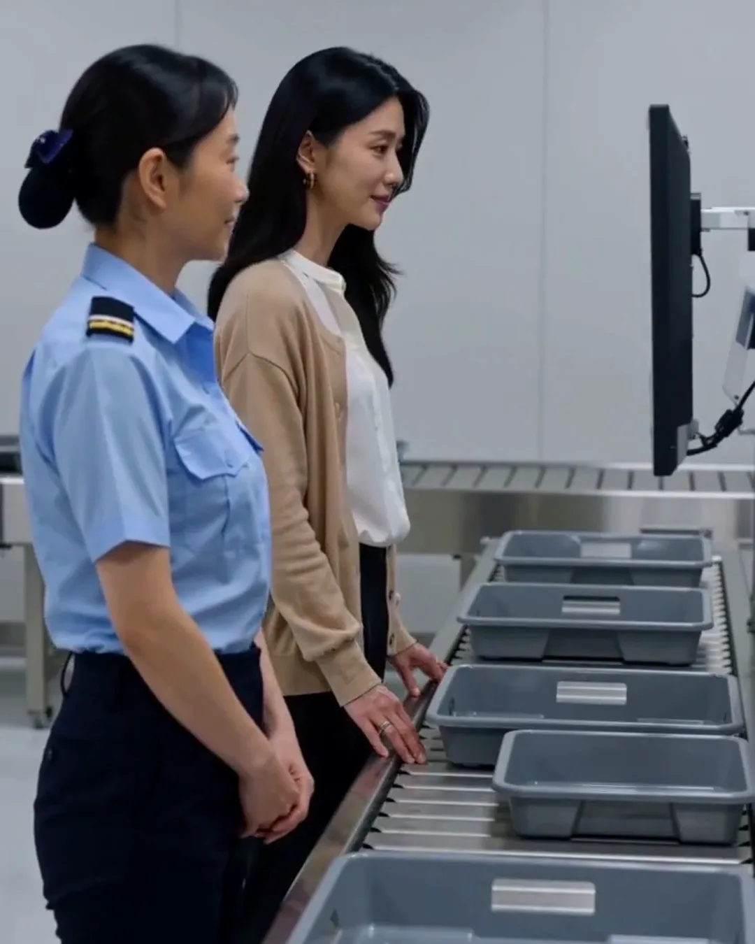空港の保安検査場で、検査員の女性と外国人の女性乗客がトレーの前で話している