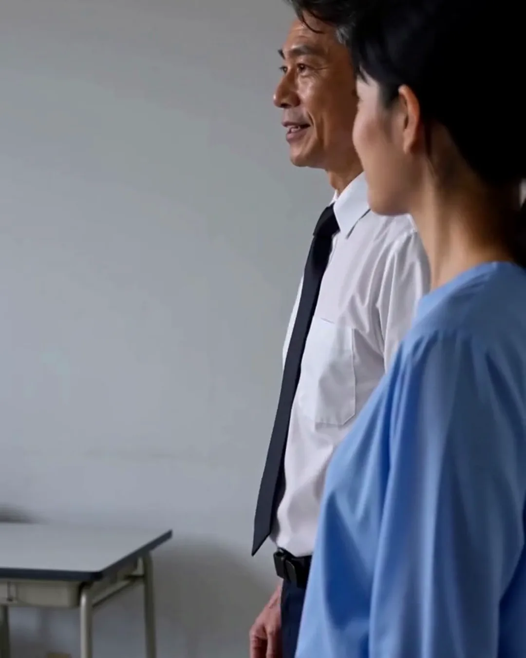 自動車教習所の教室で、教官の男性と外国人の男性教習生が机を挟んで話している