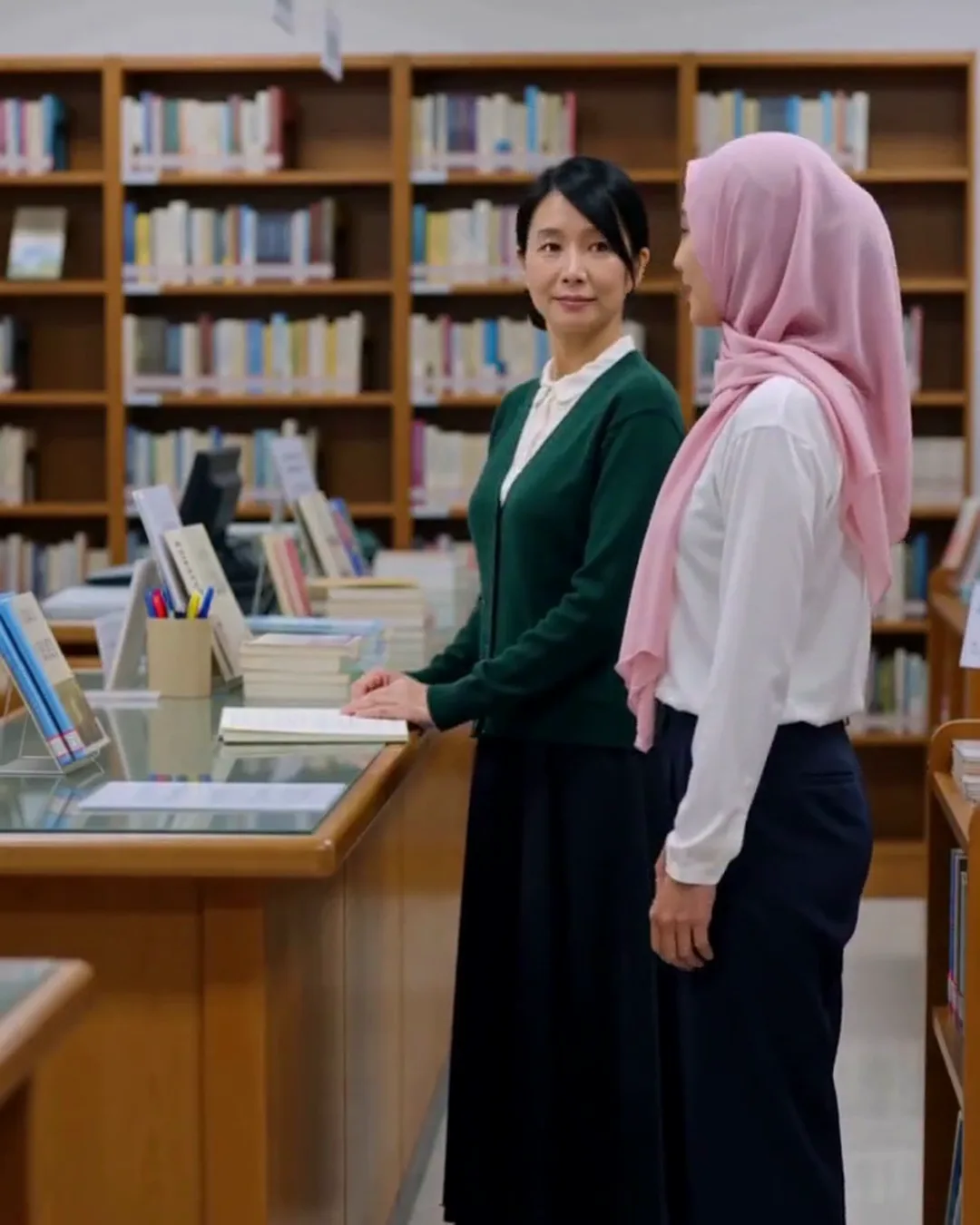 図書館のカウンターで、司書と外国人の若い女性が本を前に話している