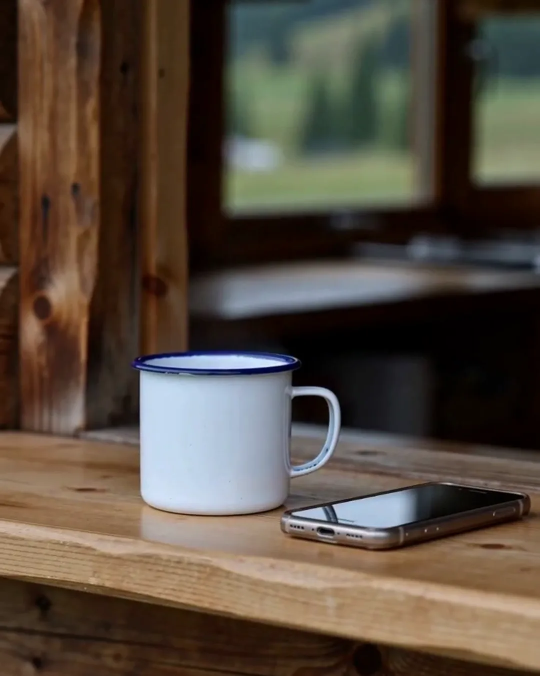 山小屋の木のカウンターに置かれた、白いホーローのマグカップとスマートフォン