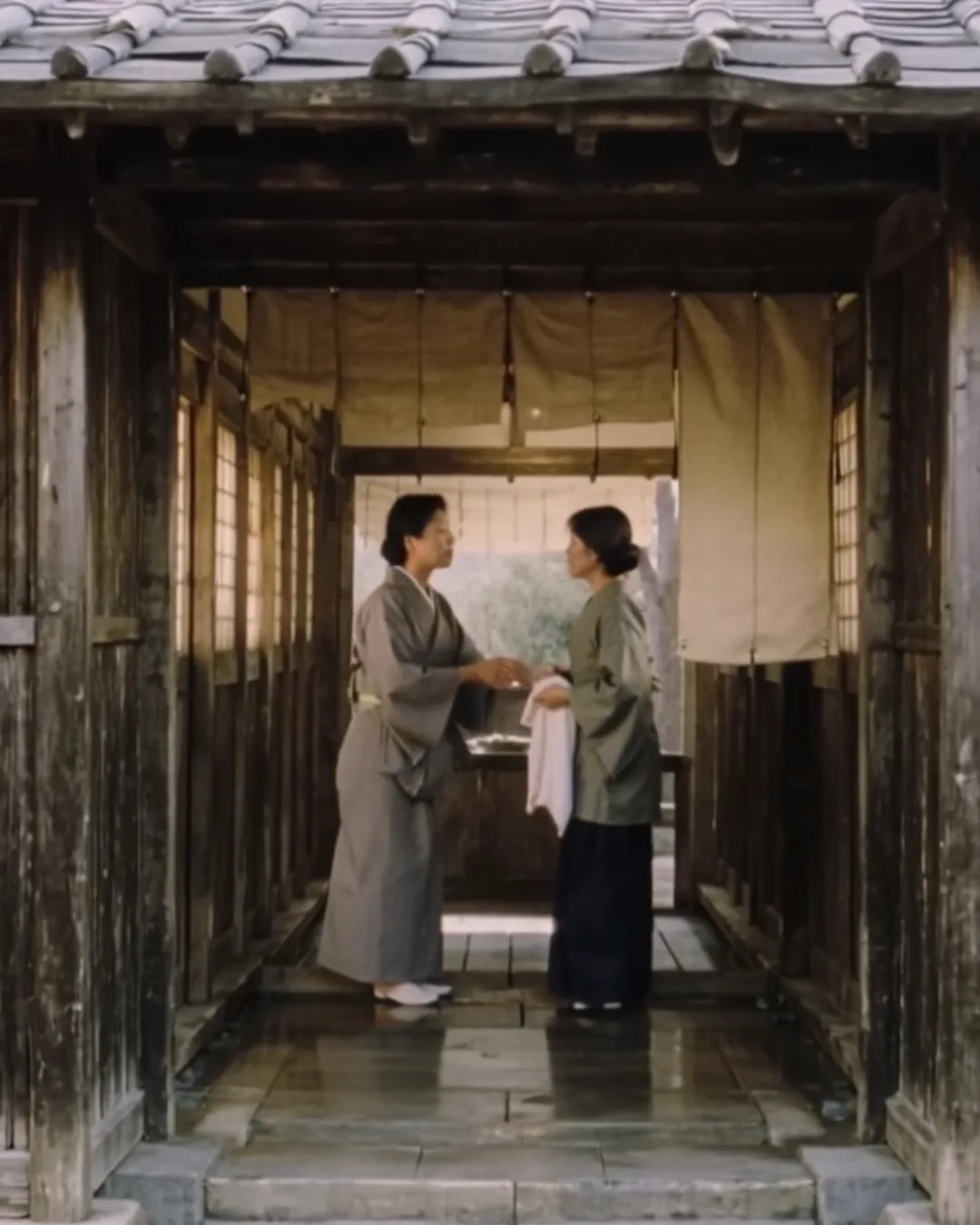 旅館の大浴場の入口で、着物姿の女性スタッフがタオルを持った外国人の女性客と話している