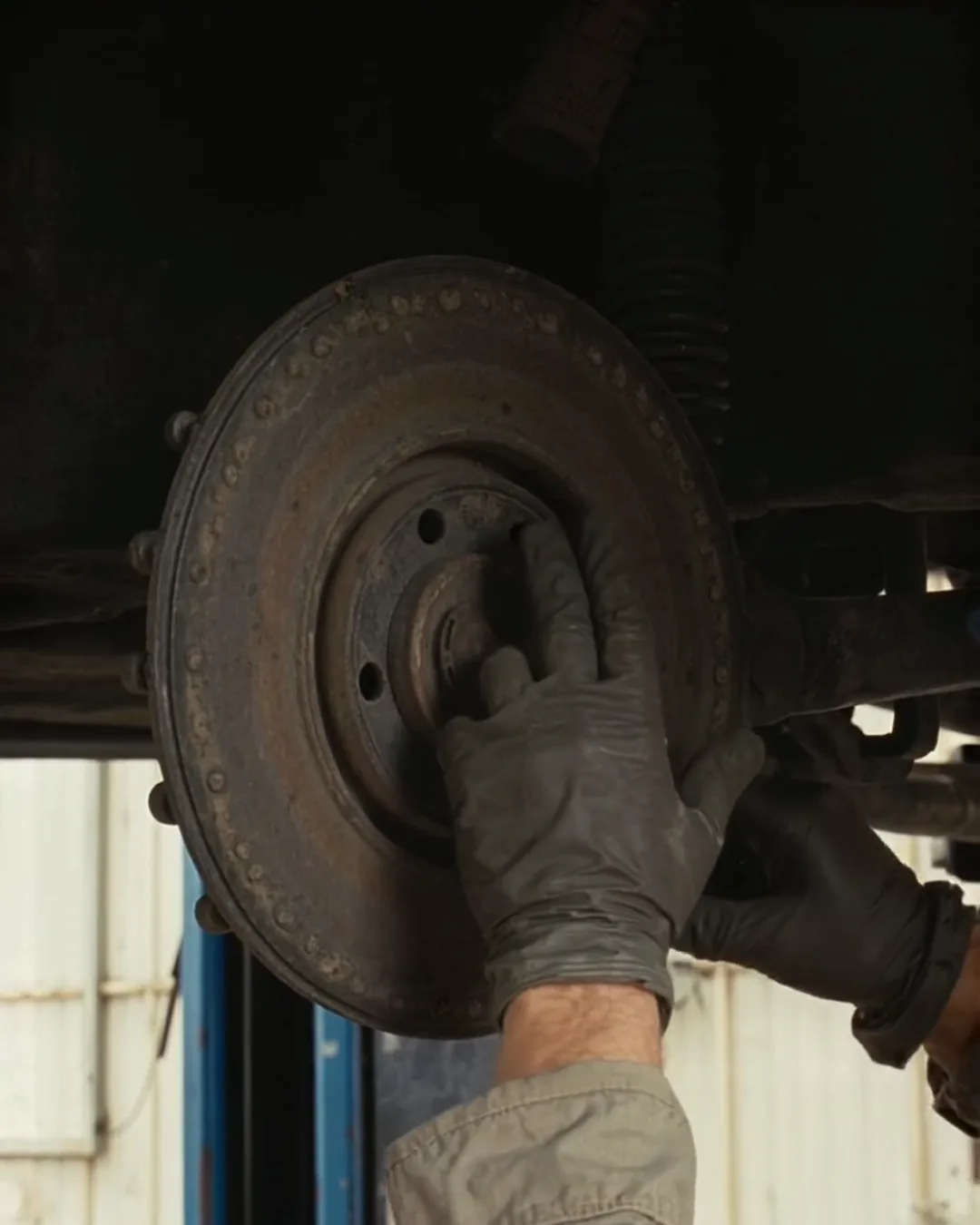 リフトに上げた車のタイヤの奥、すり減ったブレーキのディスクを整備士の手が指さしている