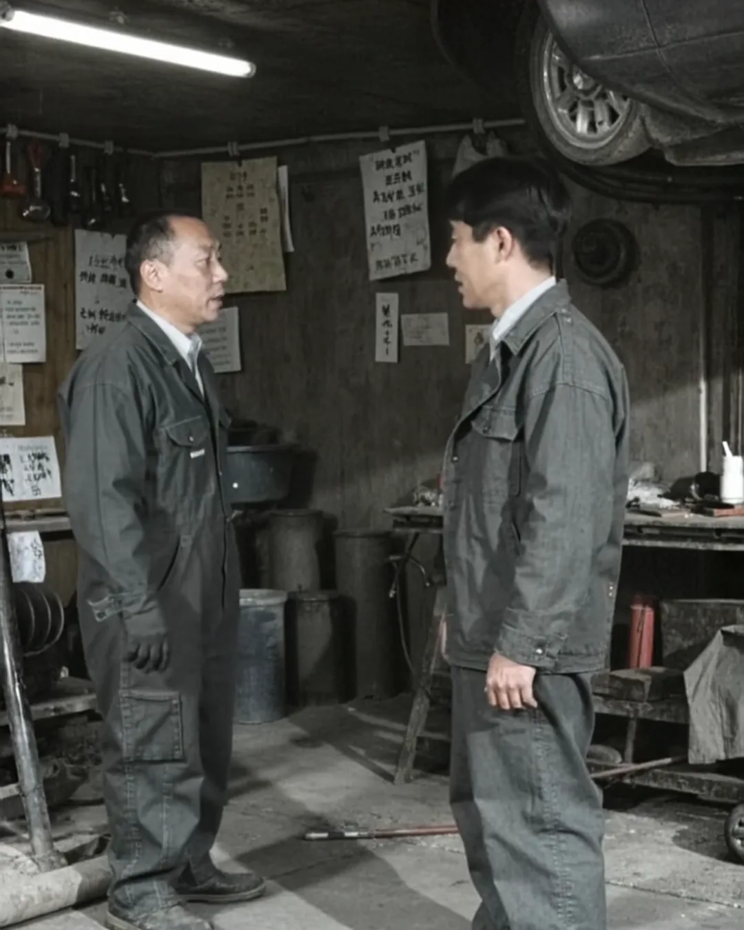整備工場でリフトに上げた車のそばに、整備士と外国人のお客様が立って話している